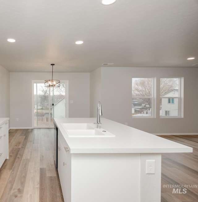 kitchen featuring a kitchen island with sink, white cabinets, sink, hanging light fixtures, and light hardwood / wood-style floors