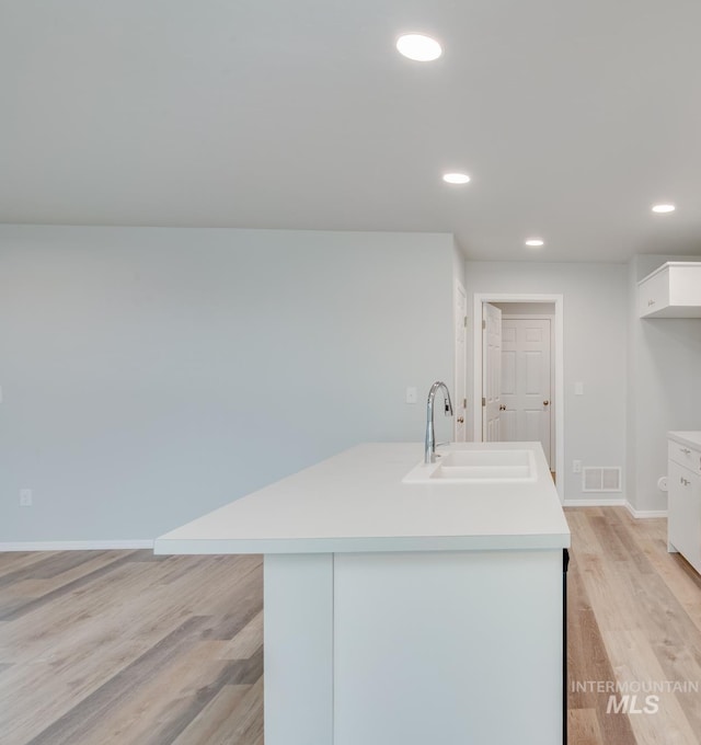 kitchen featuring a kitchen island with sink, sink, white cabinets, and light hardwood / wood-style flooring