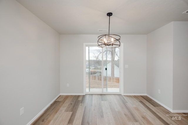 unfurnished dining area featuring light wood-type flooring and a notable chandelier