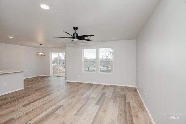 empty room featuring ceiling fan with notable chandelier, light hardwood / wood-style flooring, and a wealth of natural light