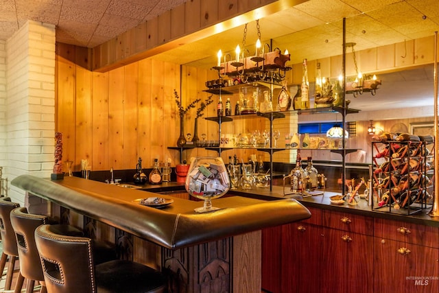 bar with sink, wood walls, pendant lighting, and brick wall