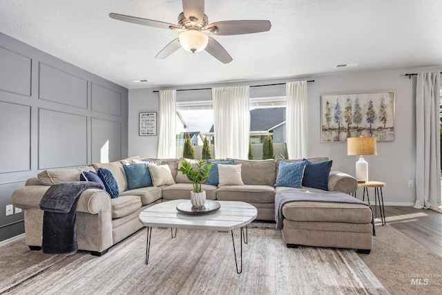 living room with a decorative wall, a ceiling fan, baseboards, and light wood finished floors