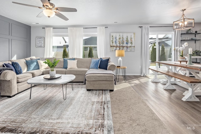 living area with visible vents, ceiling fan with notable chandelier, baseboards, and wood finished floors