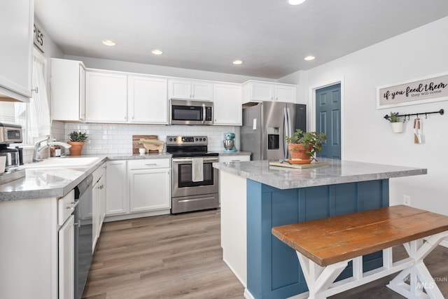 kitchen with a sink, backsplash, a center island, stainless steel appliances, and white cabinets