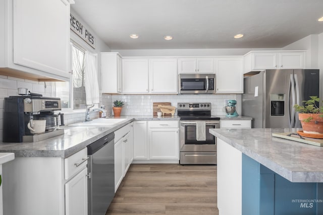 kitchen featuring light wood finished floors, white cabinets, stainless steel appliances, and a sink