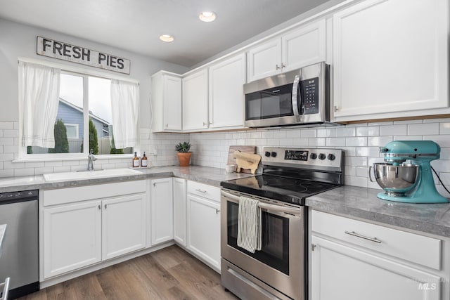 kitchen featuring wood finished floors, a sink, stainless steel appliances, white cabinets, and backsplash