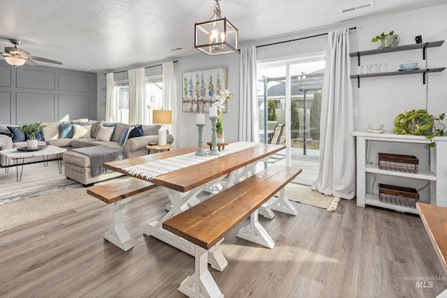 dining area with visible vents, ceiling fan with notable chandelier, a decorative wall, and wood finished floors