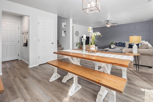 dining room featuring stairway, ceiling fan with notable chandelier, light wood-style flooring, and a decorative wall