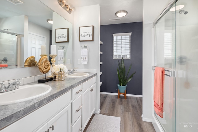 full bath featuring double vanity, wood finished floors, a stall shower, and a sink