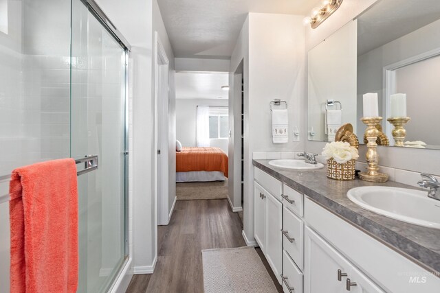 ensuite bathroom with a sink, a stall shower, wood finished floors, and double vanity