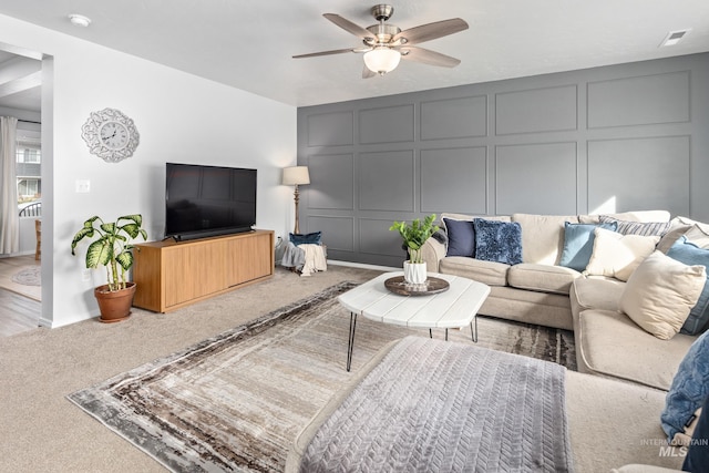 living room featuring a decorative wall, carpet flooring, and ceiling fan