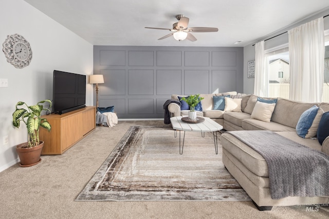 living room featuring a decorative wall, carpet, baseboards, and ceiling fan