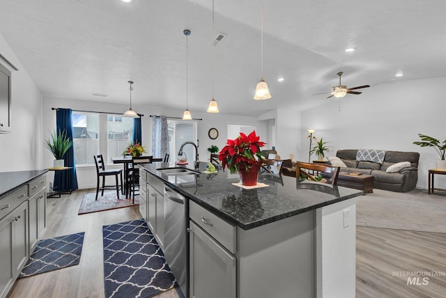 kitchen with a sink, light wood-type flooring, gray cabinets, stainless steel dishwasher, and a kitchen island with sink