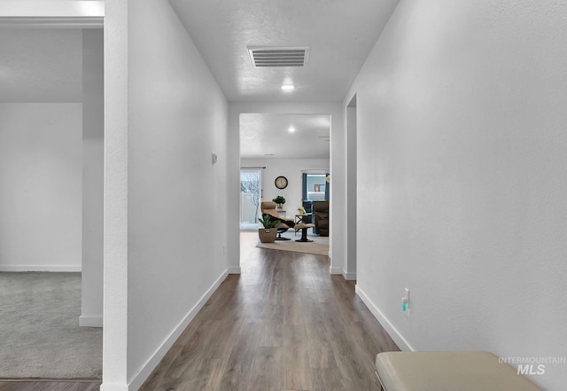 hallway with visible vents, baseboards, and wood finished floors