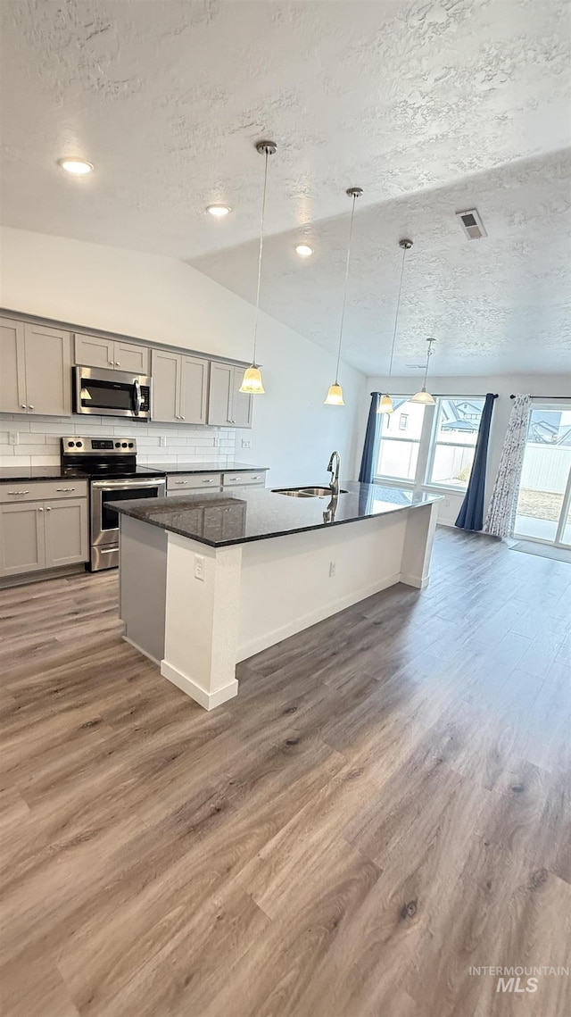 kitchen featuring wood finished floors, visible vents, stainless steel appliances, dark countertops, and tasteful backsplash