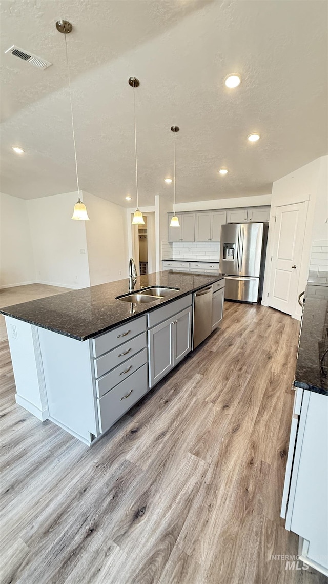 kitchen with visible vents, an island with sink, light wood-style floors, stainless steel appliances, and a sink