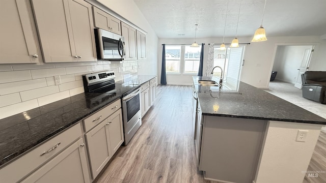 kitchen with a sink, decorative backsplash, gray cabinets, appliances with stainless steel finishes, and a kitchen island with sink