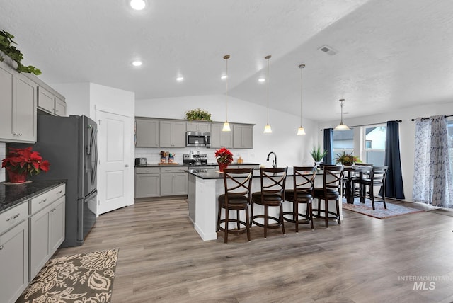 kitchen featuring visible vents, a kitchen bar, gray cabinets, appliances with stainless steel finishes, and light wood-style floors