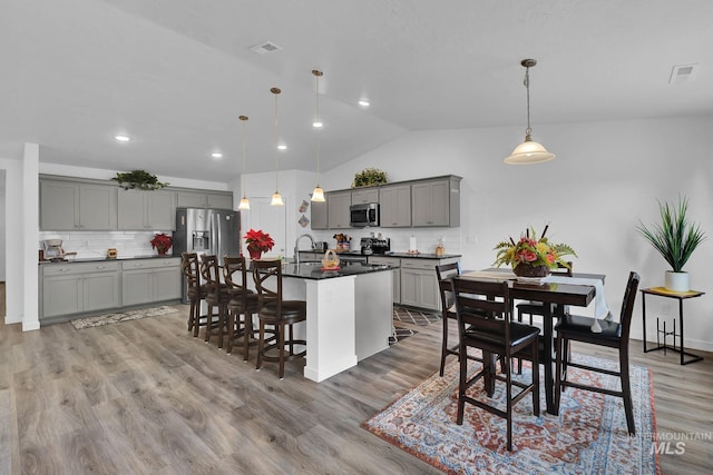 kitchen featuring gray cabinetry, dark countertops, light wood-style floors, appliances with stainless steel finishes, and vaulted ceiling