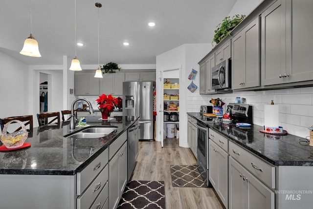 kitchen with gray cabinetry, a sink, backsplash, appliances with stainless steel finishes, and light wood finished floors