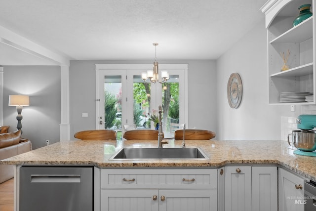 kitchen featuring stainless steel dishwasher, a sink, a chandelier, and light stone counters