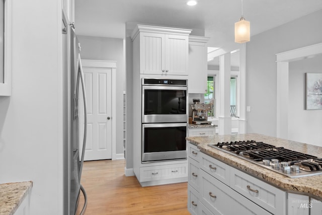 kitchen with stainless steel appliances, white cabinets, light wood-style floors, pendant lighting, and light stone counters