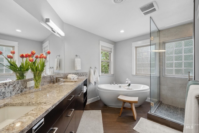 full bathroom featuring double vanity, wood finished floors, a stall shower, a freestanding bath, and baseboards