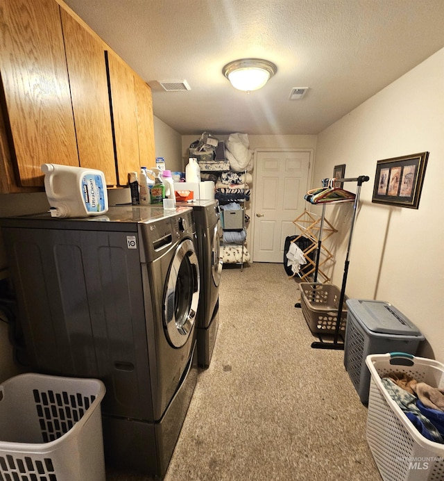 clothes washing area featuring separate washer and dryer, light colored carpet, cabinets, and a textured ceiling