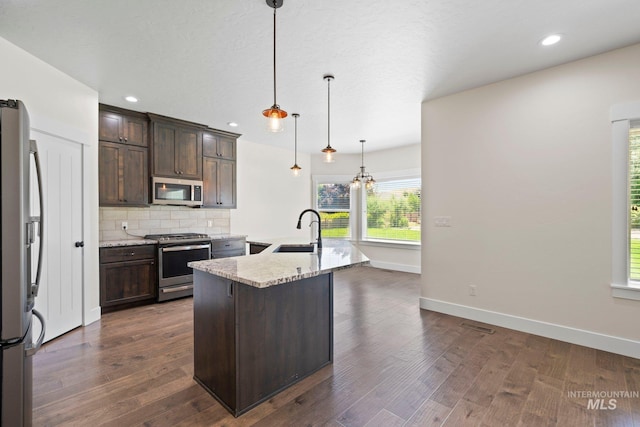 7253 River View Dr, Marsing, ID 83639 - kitchen with appliances with stainless steel finishes, dark brown cabinetry, decorative backsplash, light stone countertops, and an island with sink