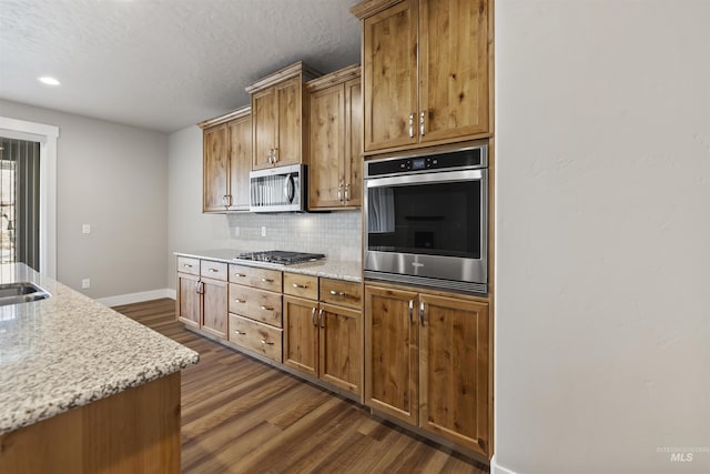 kitchen featuring light stone counters, stainless steel appliances, decorative backsplash, baseboards, and dark wood-style flooring