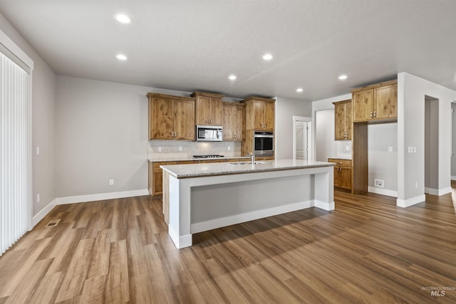 kitchen with stainless steel microwave, a sink, brown cabinetry, gas cooktop, and a kitchen island with sink