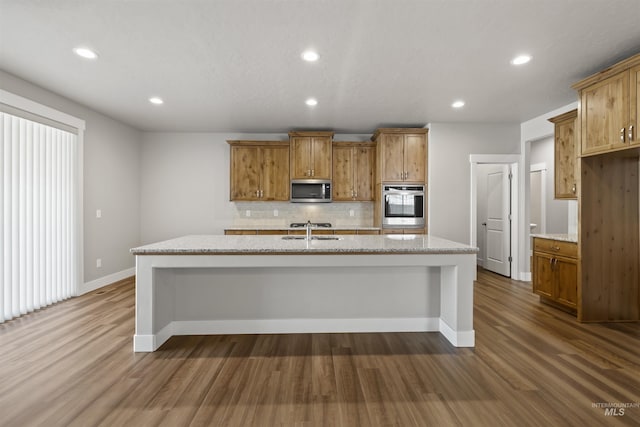 kitchen with brown cabinetry, dark wood-style flooring, a sink, decorative backsplash, and stainless steel appliances