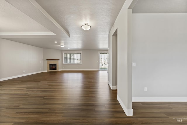 unfurnished living room featuring a tiled fireplace, a textured ceiling, baseboards, and dark wood-style flooring