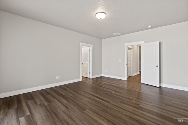 empty room with visible vents, baseboards, a textured ceiling, and dark wood-style floors