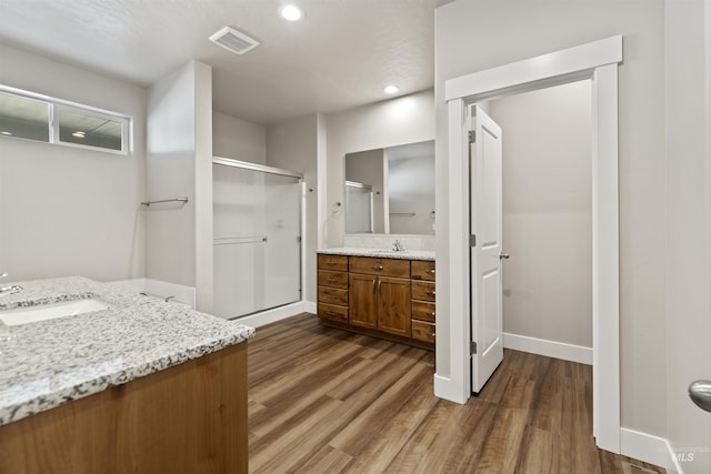 full bathroom featuring visible vents, two vanities, a stall shower, wood finished floors, and a sink