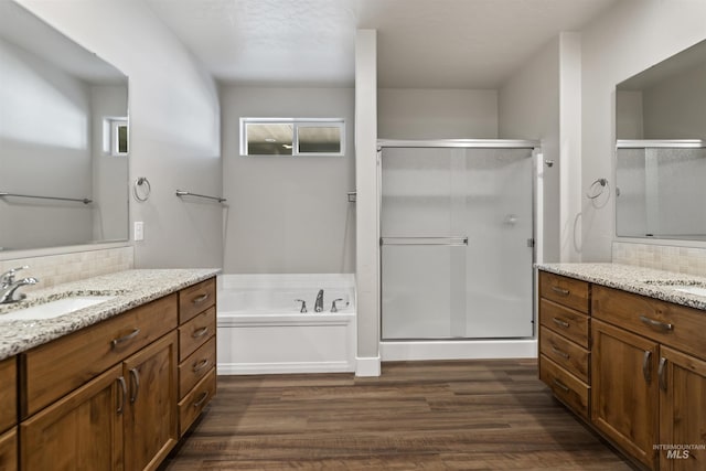 full bathroom featuring backsplash, a shower stall, two vanities, wood finished floors, and a sink