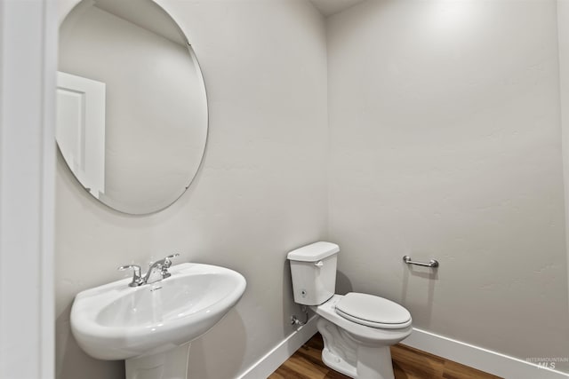 half bathroom featuring toilet, wood finished floors, baseboards, and a sink