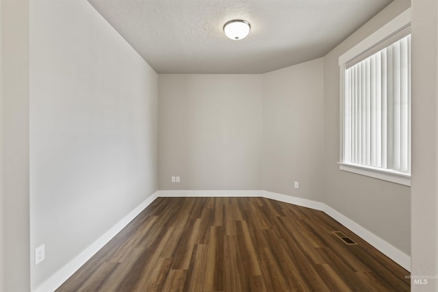 unfurnished room featuring visible vents, a textured ceiling, dark wood-type flooring, and baseboards