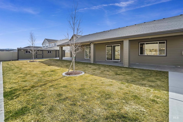 rear view of property featuring a patio, a lawn, fence, and roof with shingles