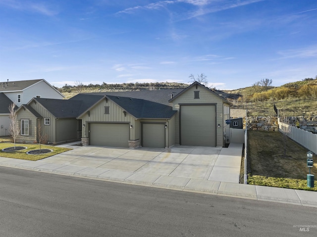 view of front facade with fence, driveway, stone siding, a garage, and board and batten siding