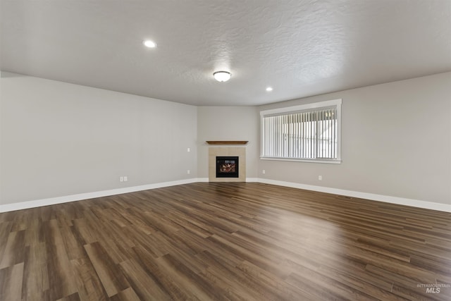 unfurnished living room featuring baseboards, recessed lighting, a tile fireplace, dark wood-style floors, and a textured ceiling