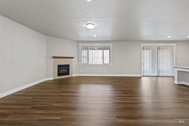 unfurnished living room with a tiled fireplace, a textured ceiling, baseboards, and dark wood-style flooring