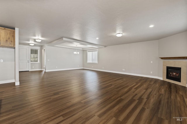 unfurnished living room with baseboards, recessed lighting, dark wood-type flooring, a tiled fireplace, and a chandelier