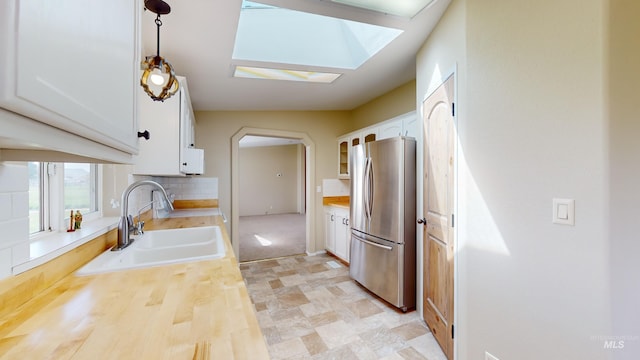 kitchen featuring white cabinetry, hanging light fixtures, stainless steel fridge, sink, and backsplash