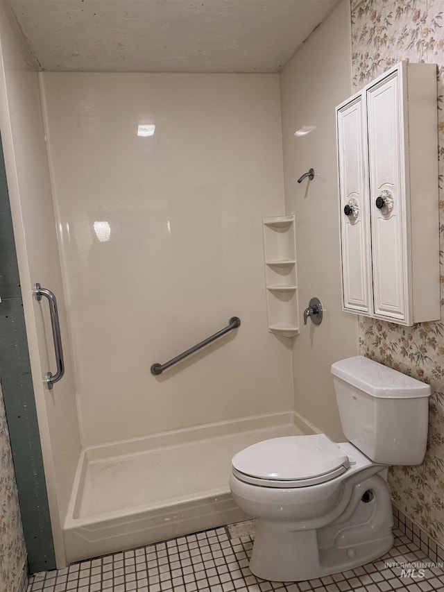 bathroom featuring toilet, wallpapered walls, tile patterned flooring, and a stall shower