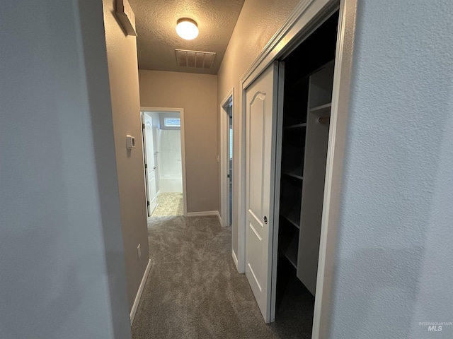 hall with a textured ceiling and dark colored carpet