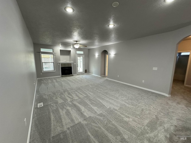 unfurnished living room featuring a textured ceiling, ceiling fan, carpet, and a tiled fireplace