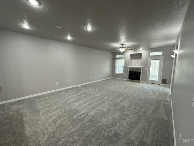 unfurnished living room with carpet floors, ceiling fan, a tile fireplace, and a textured ceiling