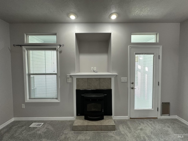 unfurnished living room with a textured ceiling, light colored carpet, a wood stove, and plenty of natural light