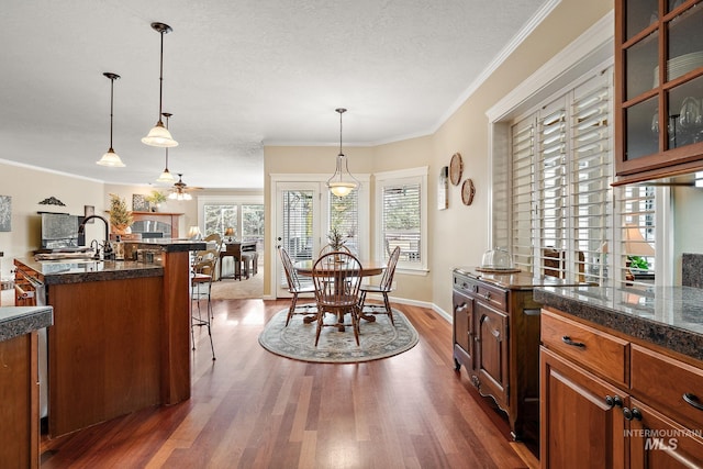 kitchen featuring a ceiling fan, glass insert cabinets, a kitchen breakfast bar, dark wood-type flooring, and crown molding